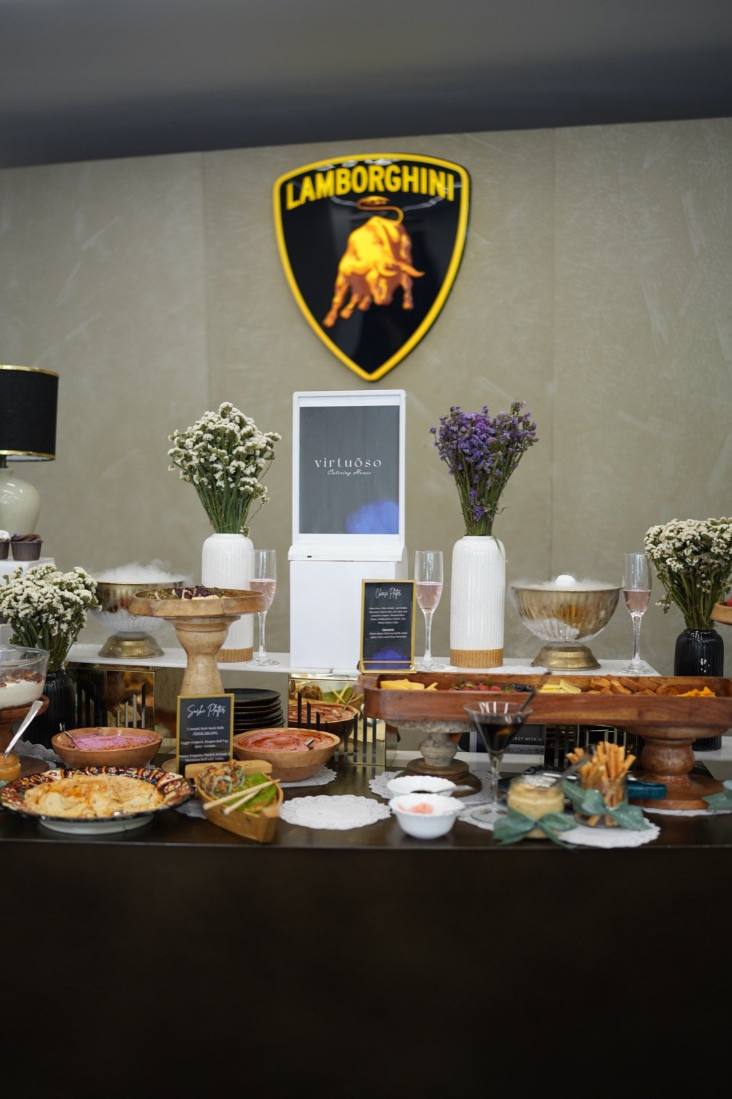 The grazing table, staged beneath the Lamborghini crest, built for circulation, not congregation.